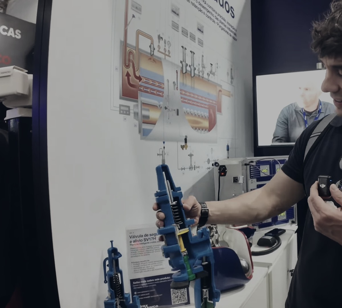 A hand presents cutaway models of safety valves next to the process diagram on the booth wall.
