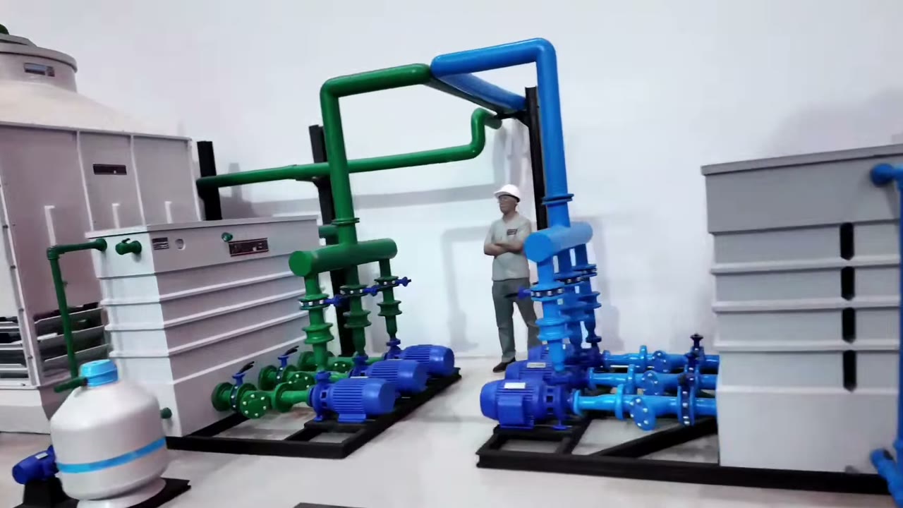Scale model of a chilled water plant: cooling tower, blue pumps and green and blue piping, with a miniature worker in a hard hat.
